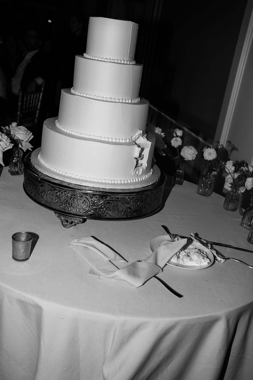 Black and white film photo of the four-tier wedding cake and a cut slice on a plate.